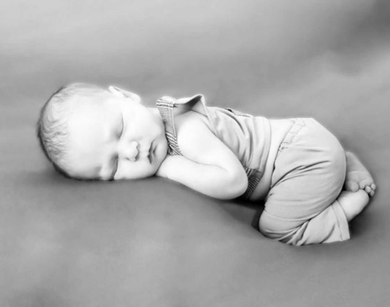 A sleeping infant in light gray clothing curled up in black and white photography.
