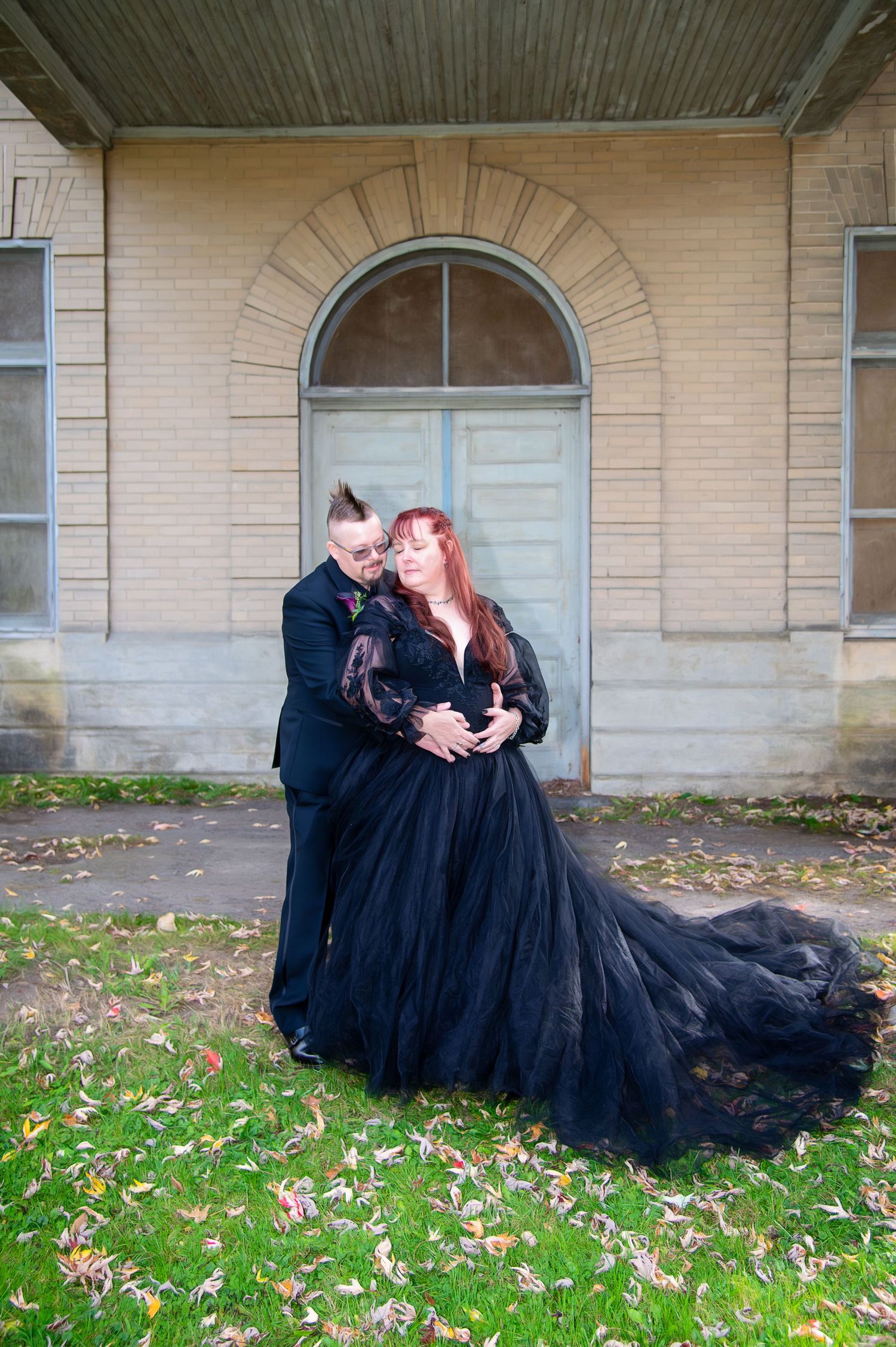 Dramatic wedding photos with couple in black attire on grass with fallen autumn leaves.
