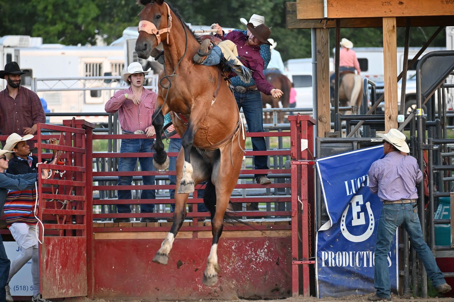 Wide view of rodeo arena showing riders competing against backdrop of trailers and spectators.