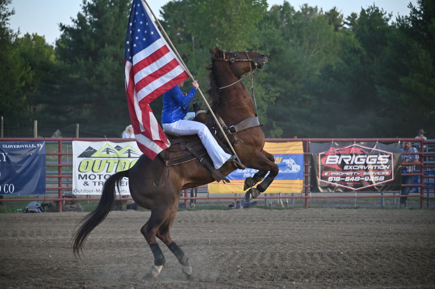 Equestrian riders carrying American flags during rodeo performance.