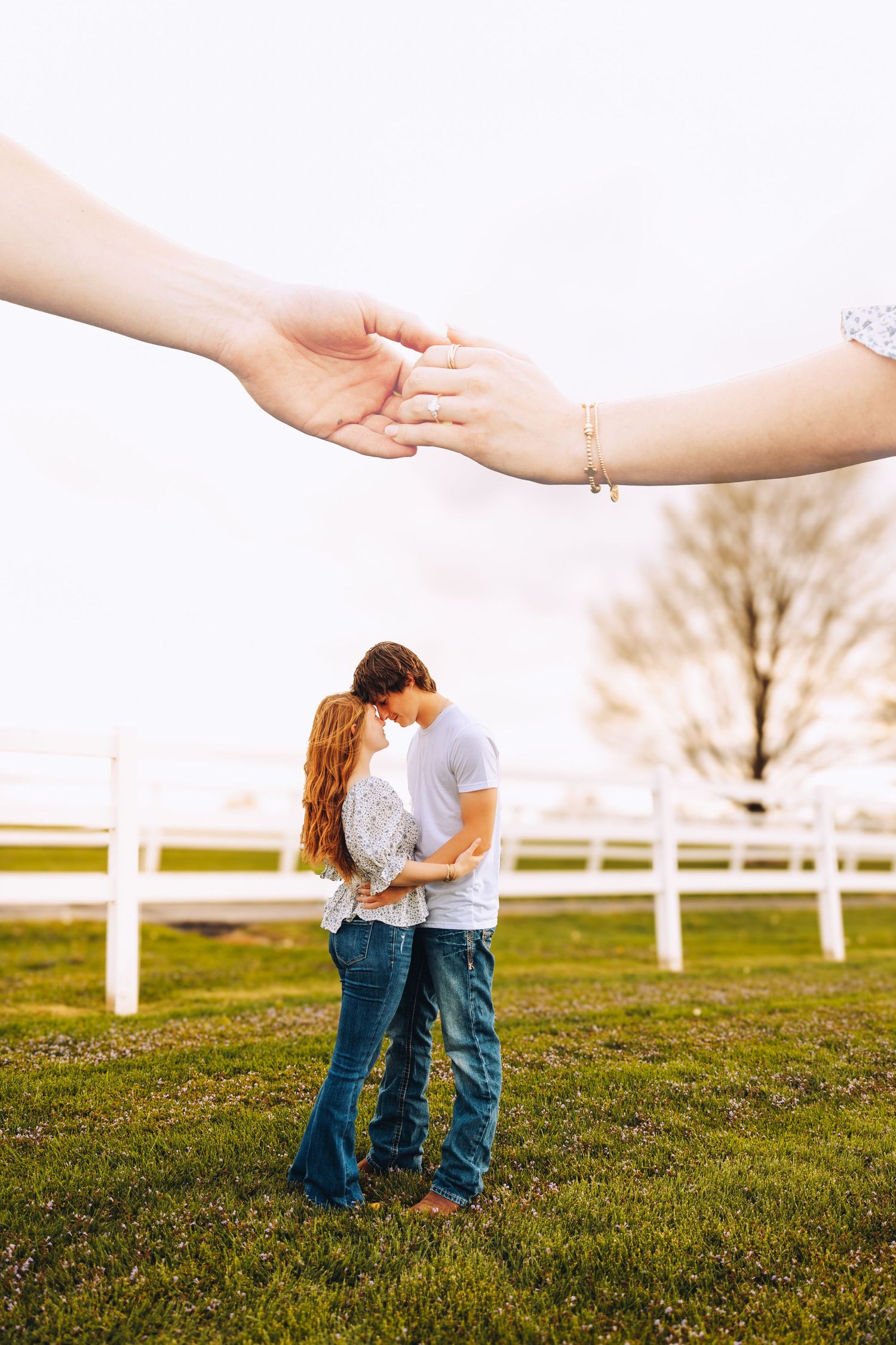 Couple shares a romantic moment on green grass as two hands reach toward each other in the foreground.
