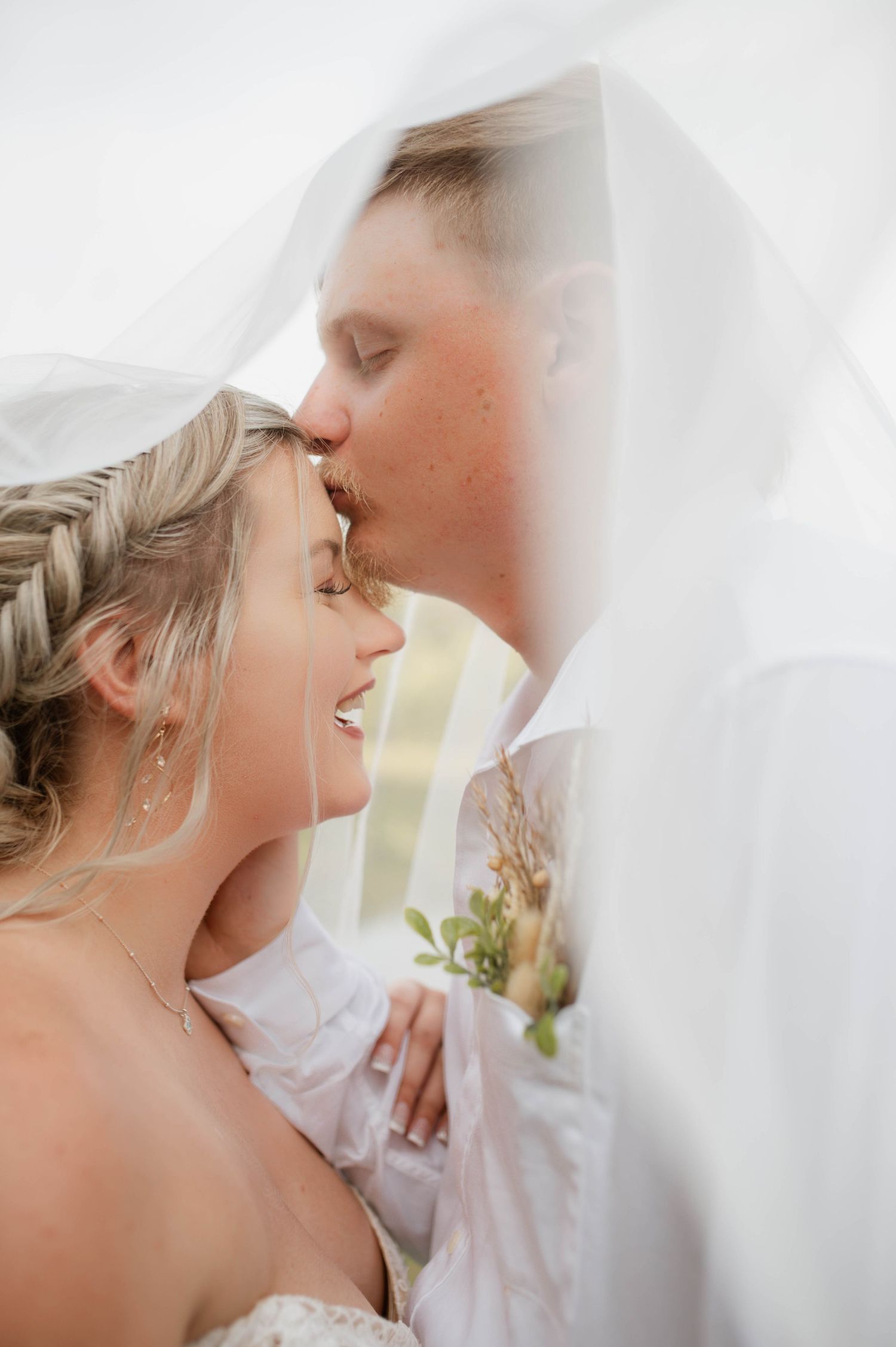 A groom kissing his bride's head.