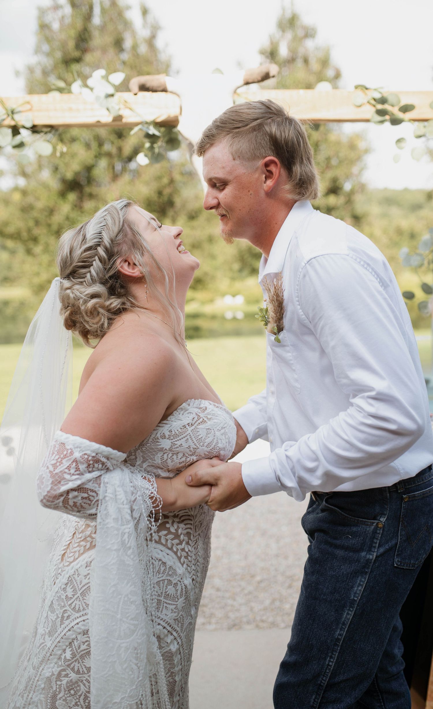 A bride and groom laughing at one another while holding hands.