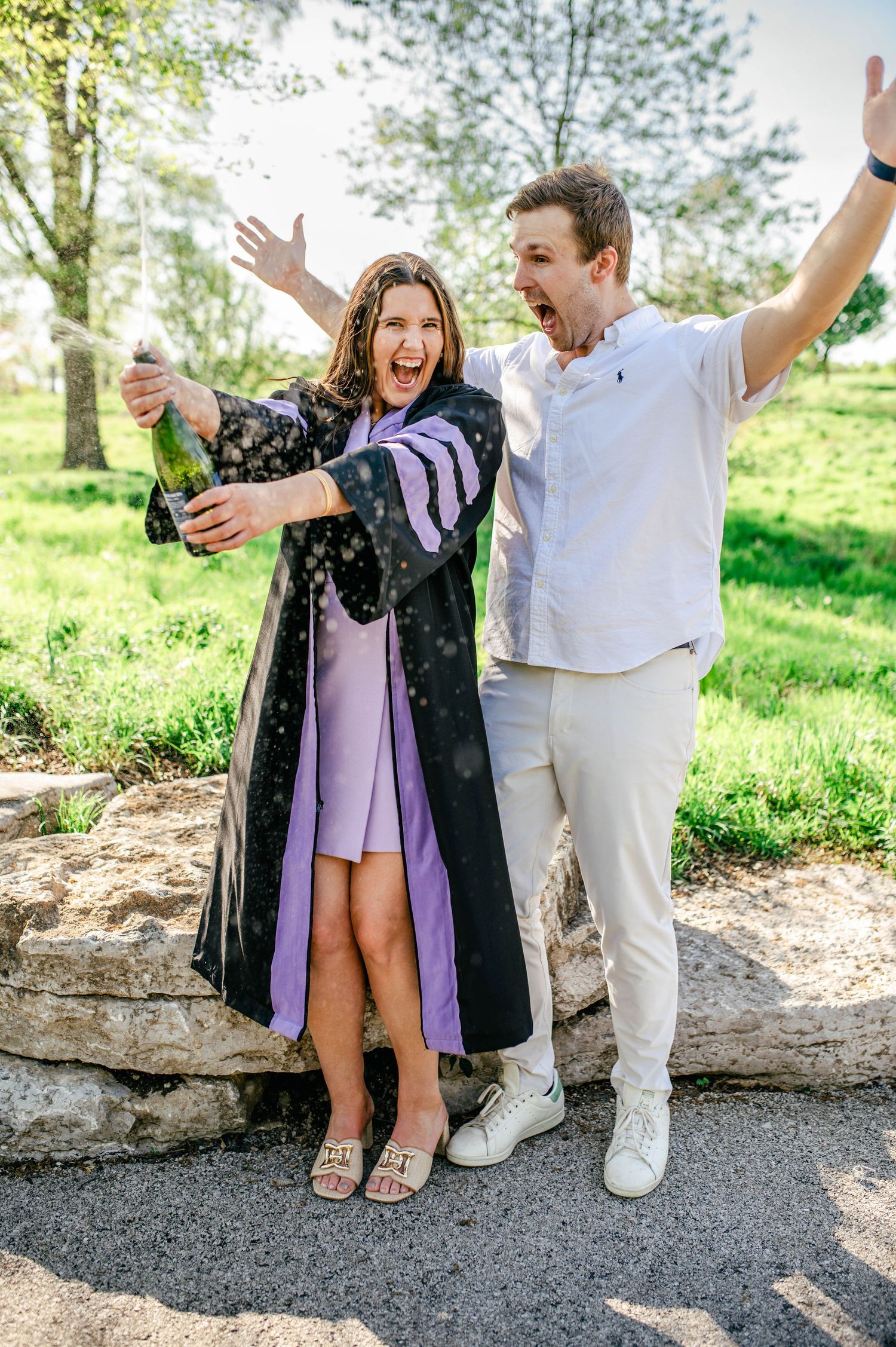 A doctoral student popping champagne while her partner smiles behind her.