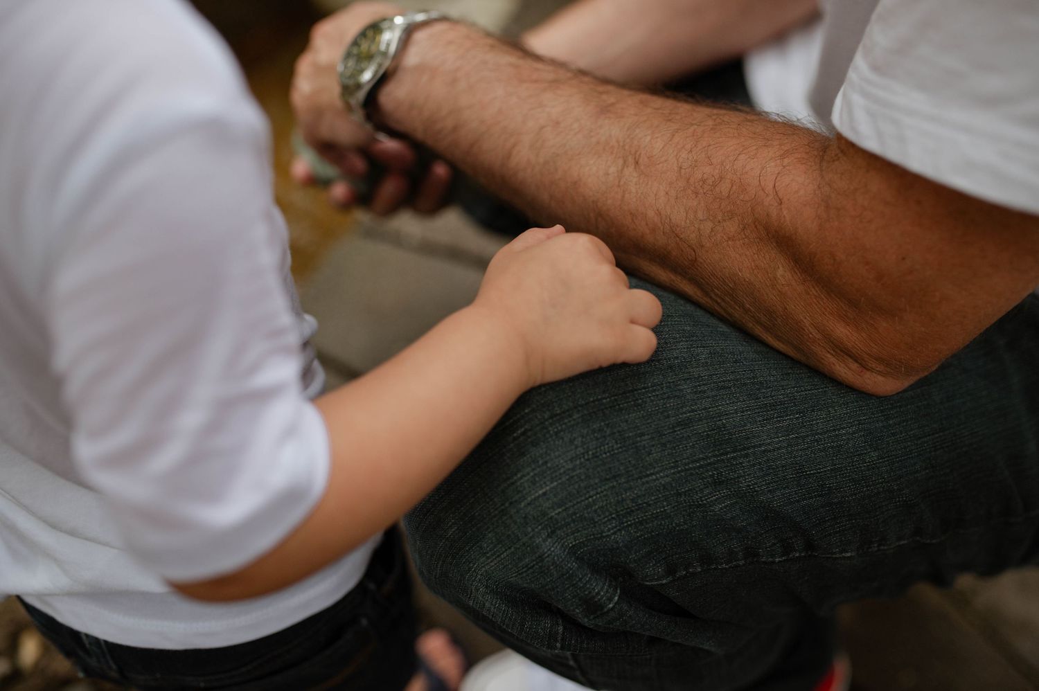 The arm of a child on his dad's leg.
