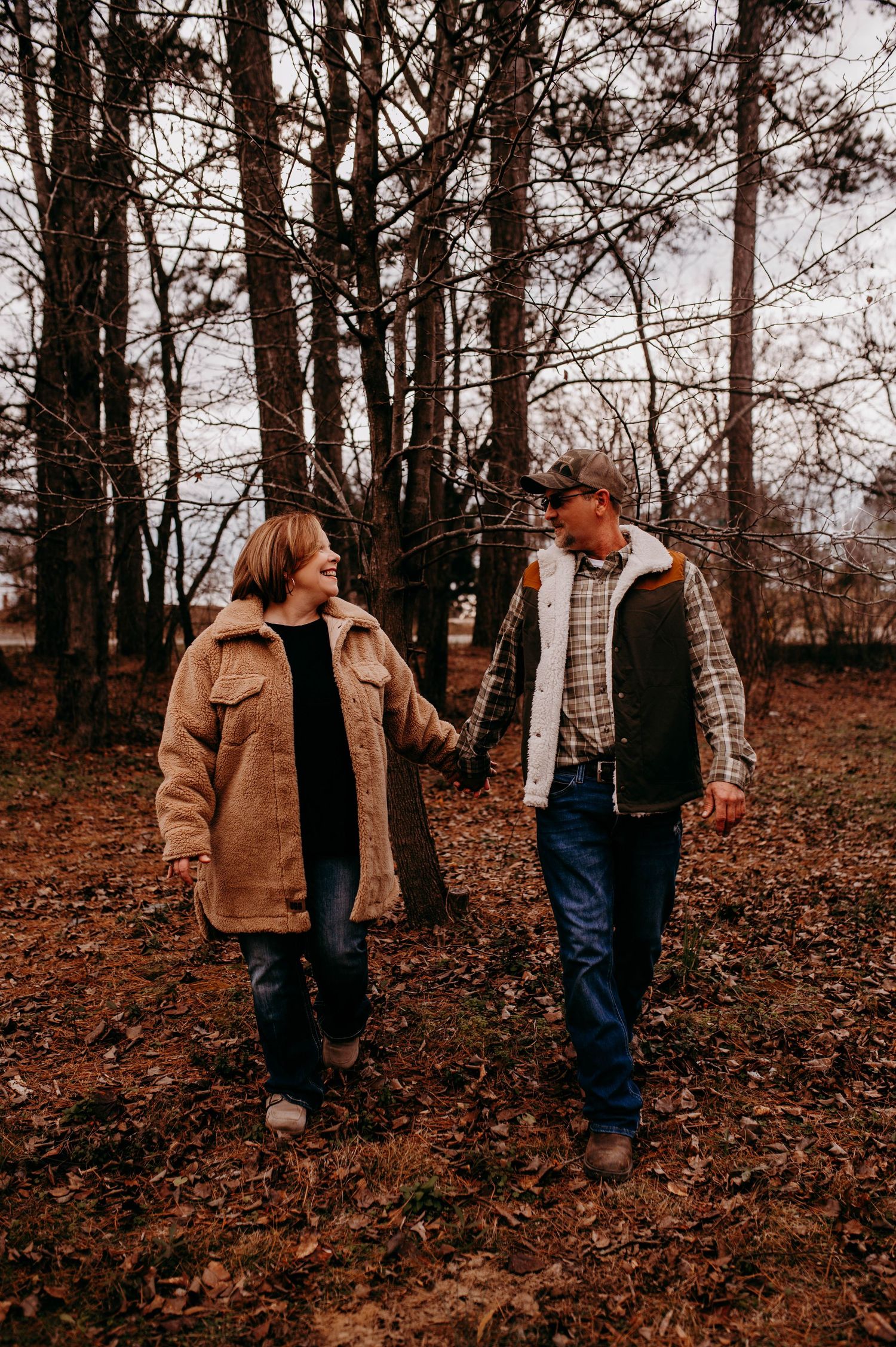 A man and woman holding hands and walking among the trees.