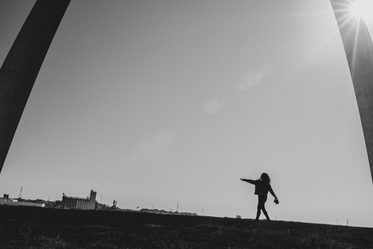 A woman holding a camera walking in front of the arch.