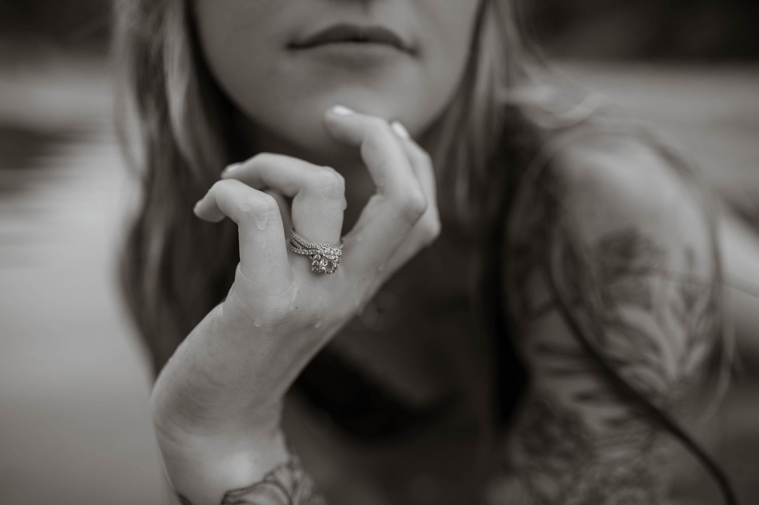 An engagement ring showcased on the hand of a woman resting her hand on her chin.