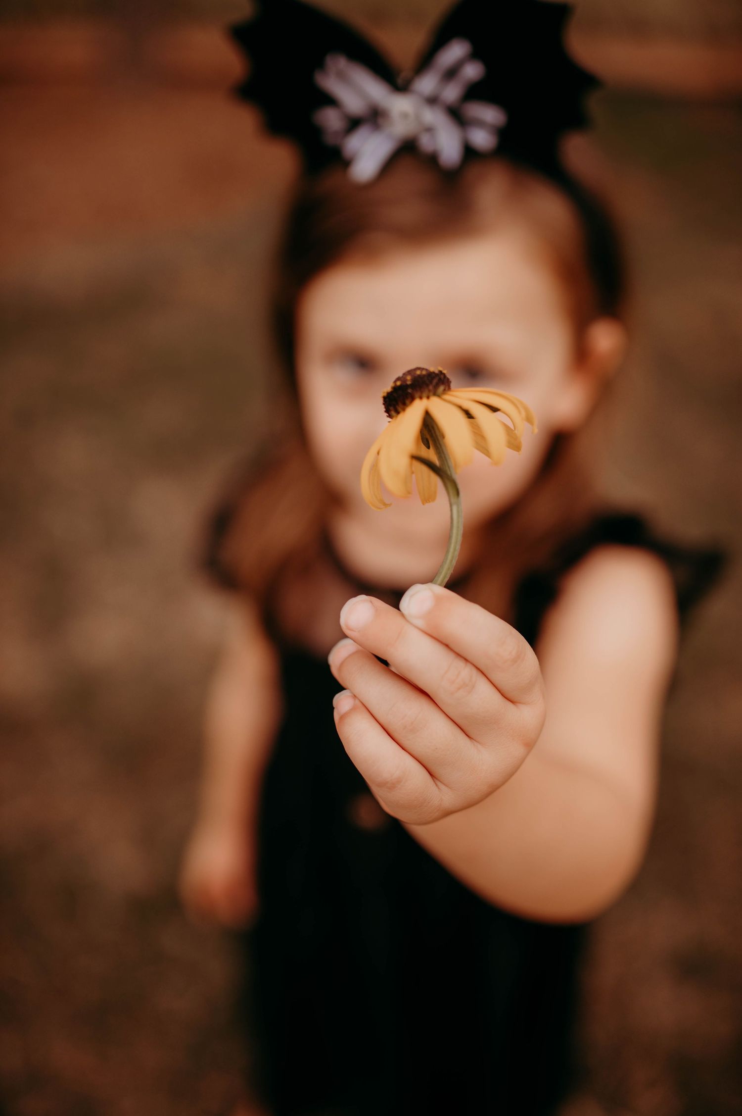 A small girl holding up a flower.