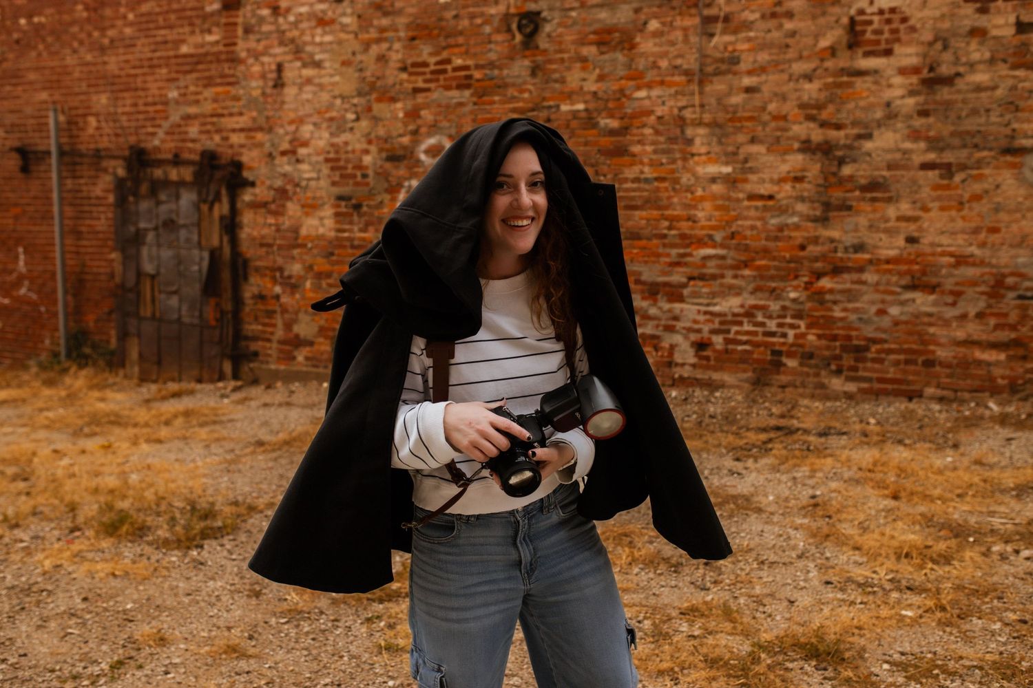 A photographer holding a camera with a jacket on her head.