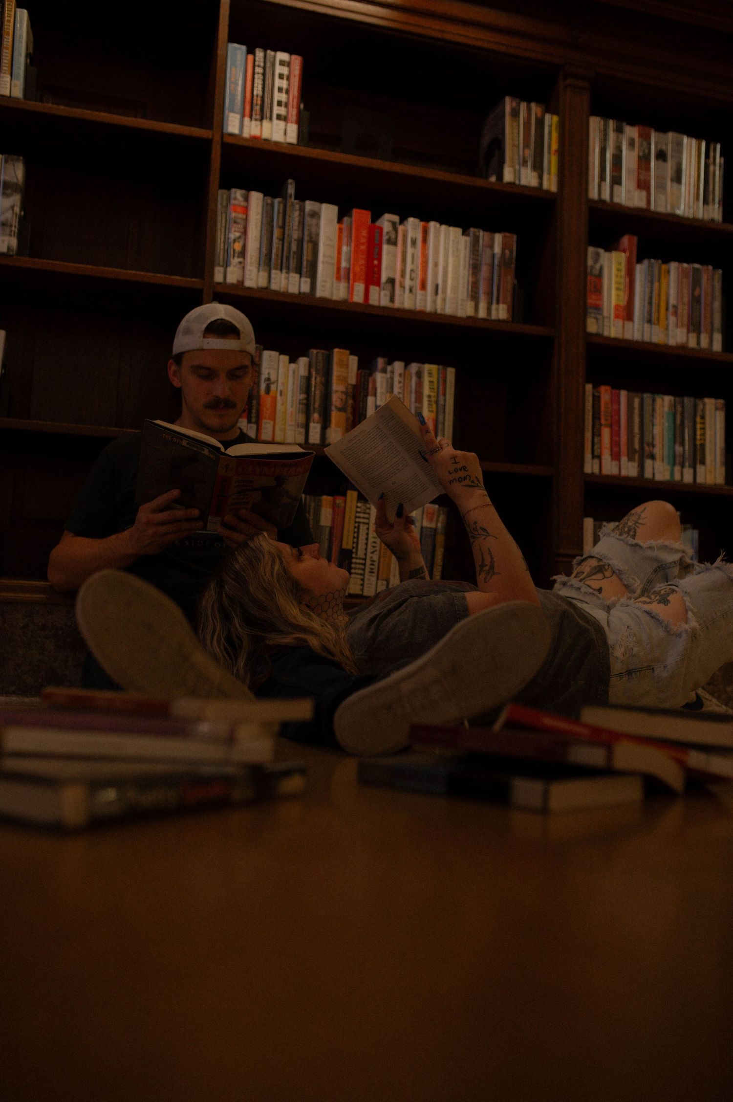 A couple reading books together on the floor of a library.