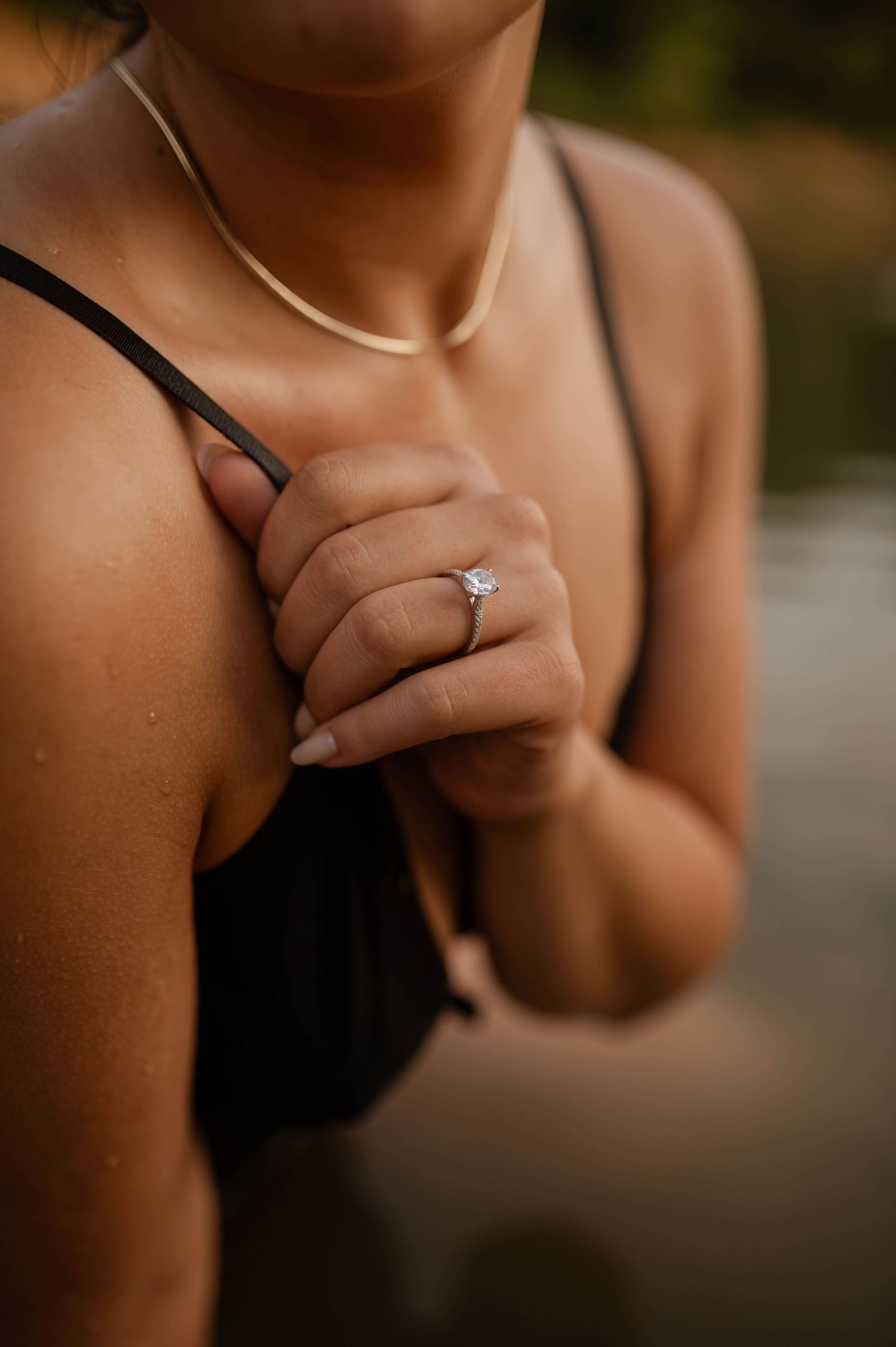 An engagement ring showcased on the hand of a woman holding the strap of her lingerie top.