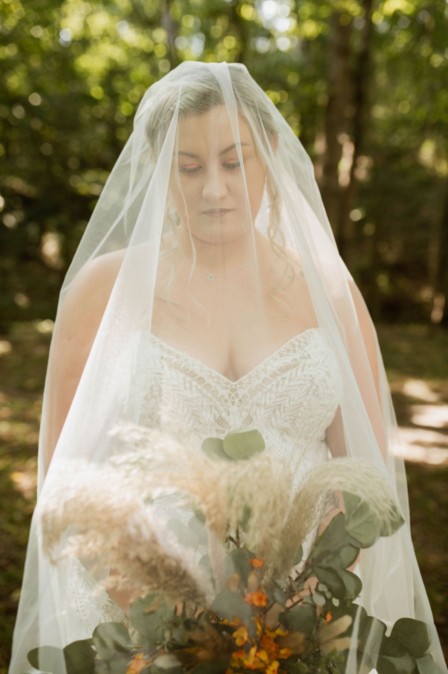 A bride looking at her flowers with her veil over her face.