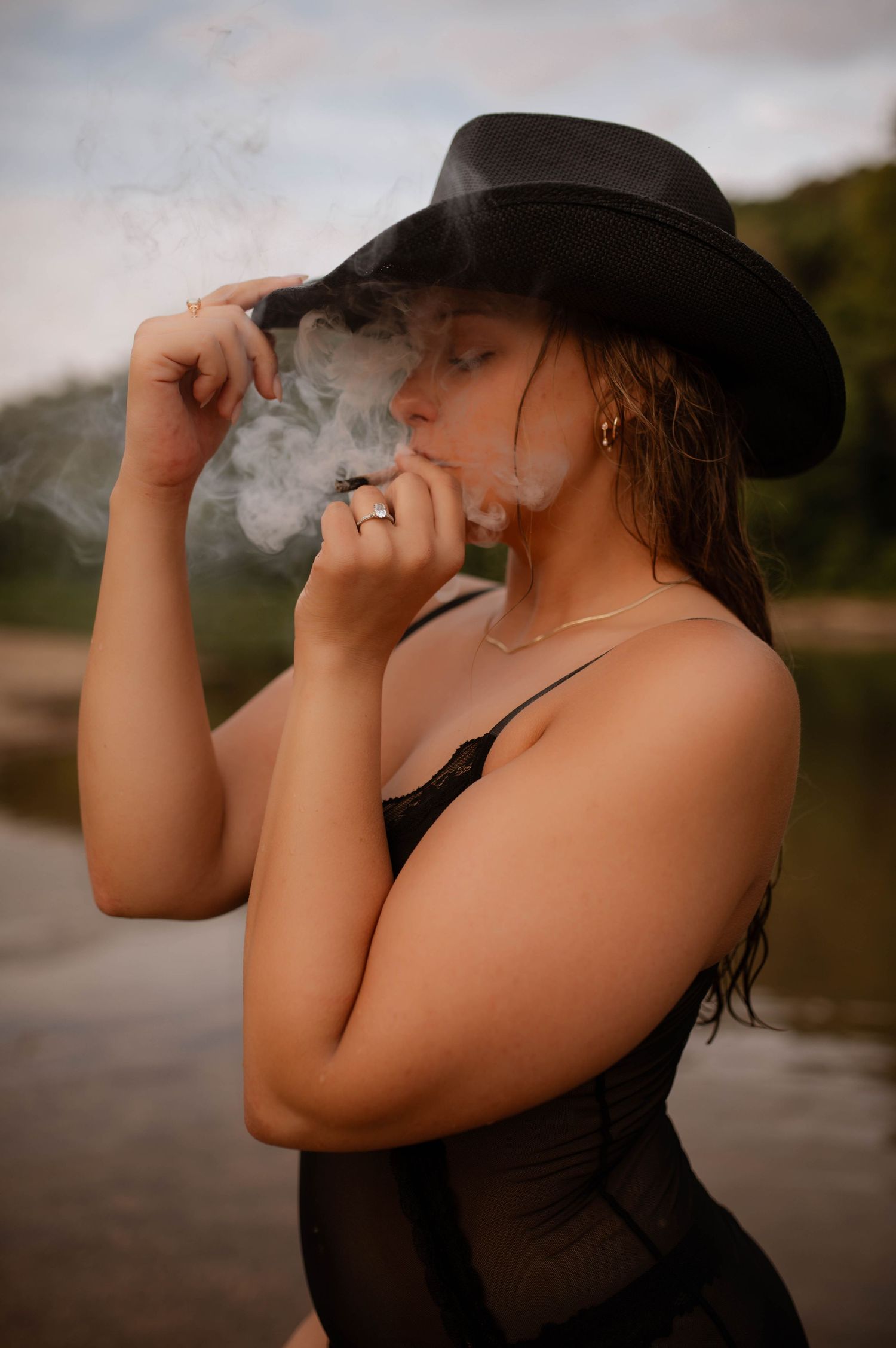 A woman smoking a joint while standing in water and wearing a cowboy hat.