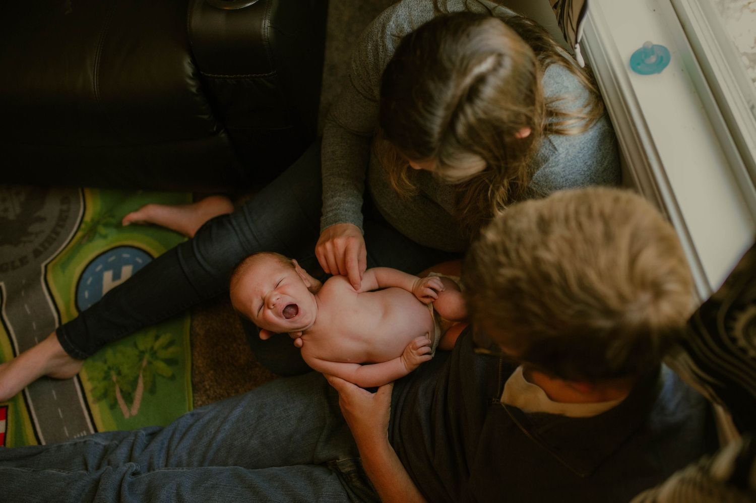 A mother and dad holding their baby who is yawning