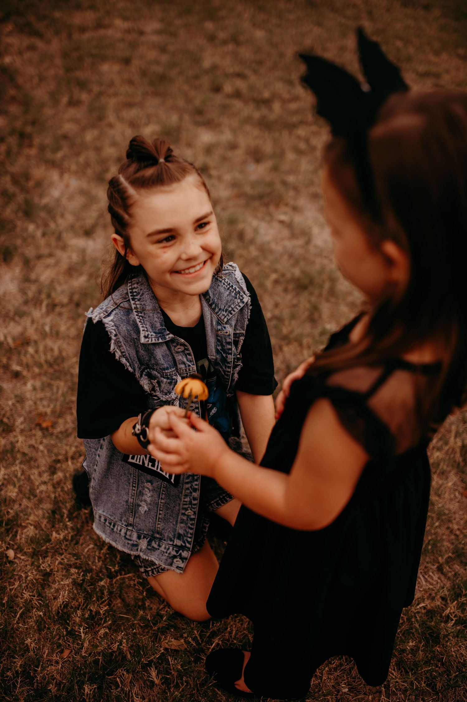 A small girl receiving a flower from her older sister, who is kneeling in front of her.