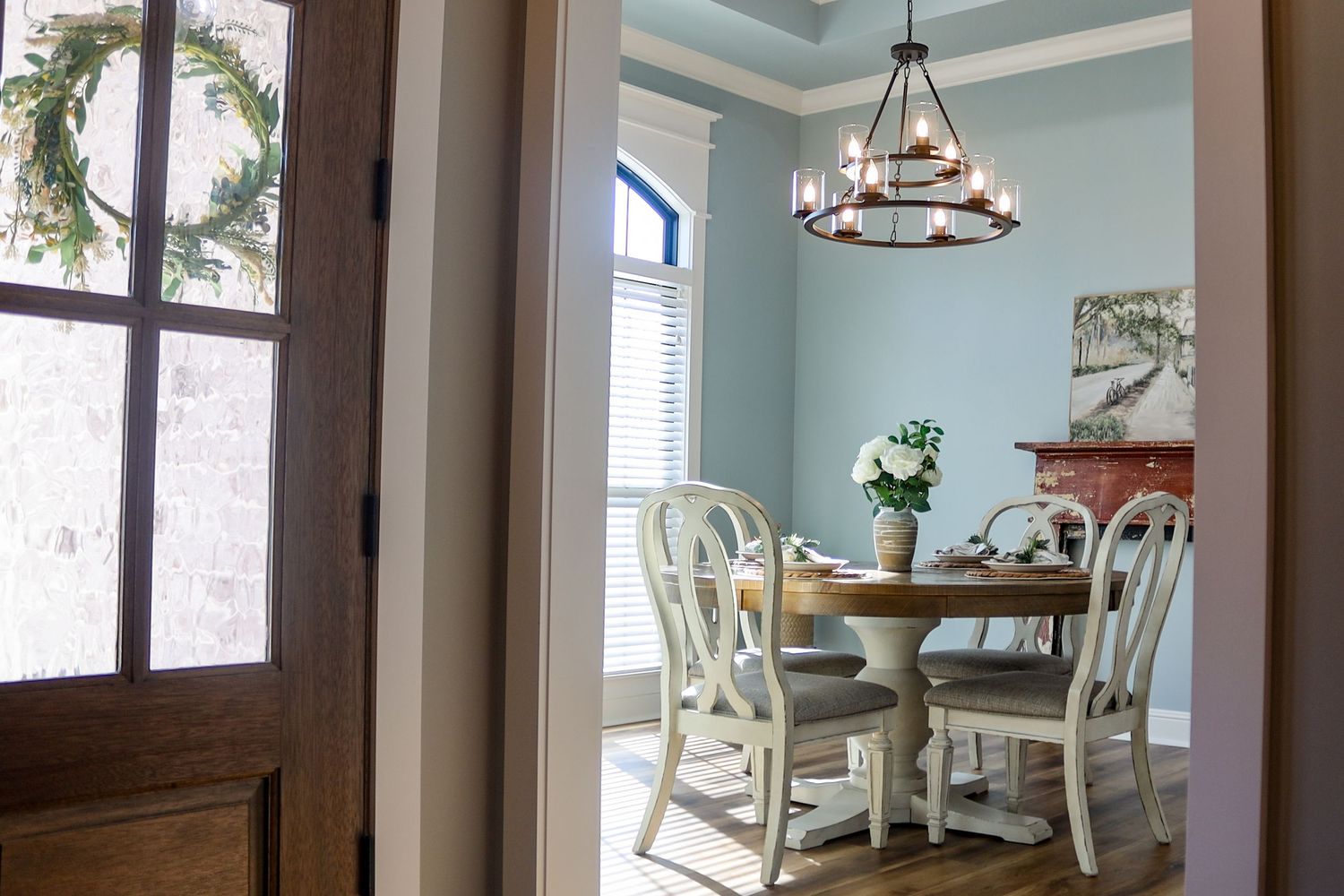 Dining area with round table and white chairs beneath rustic chandelier.