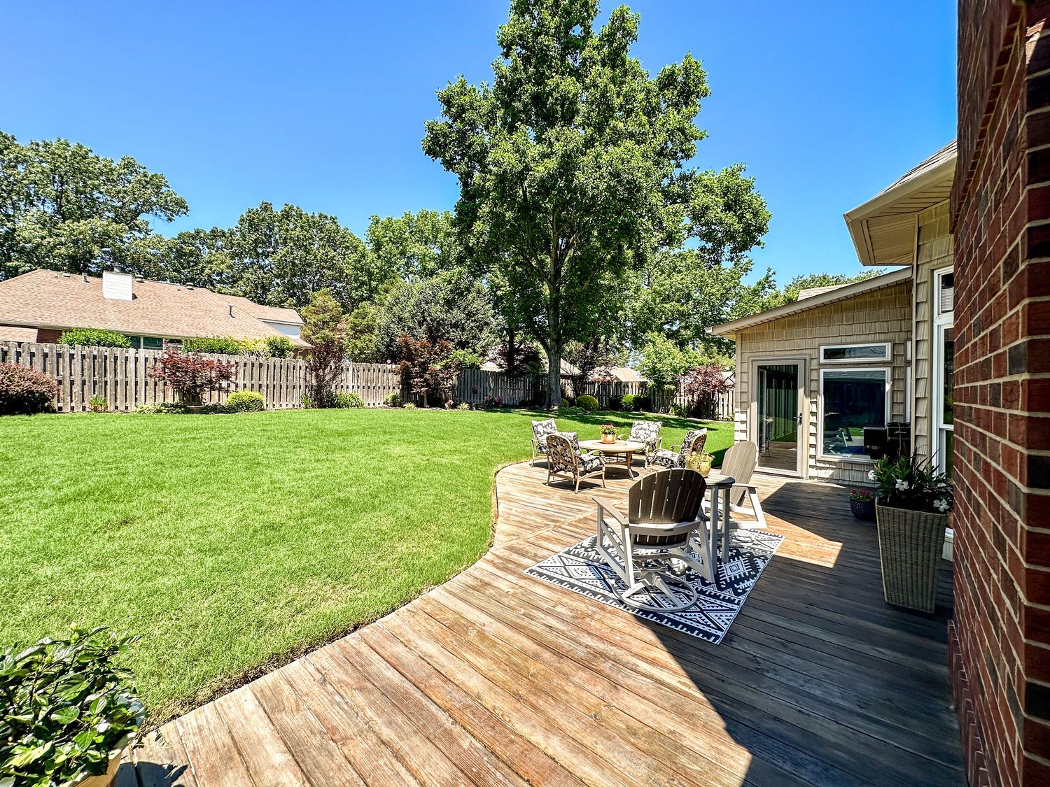 Large backyard with green lawn and covered patio area surrounded by mature trees.