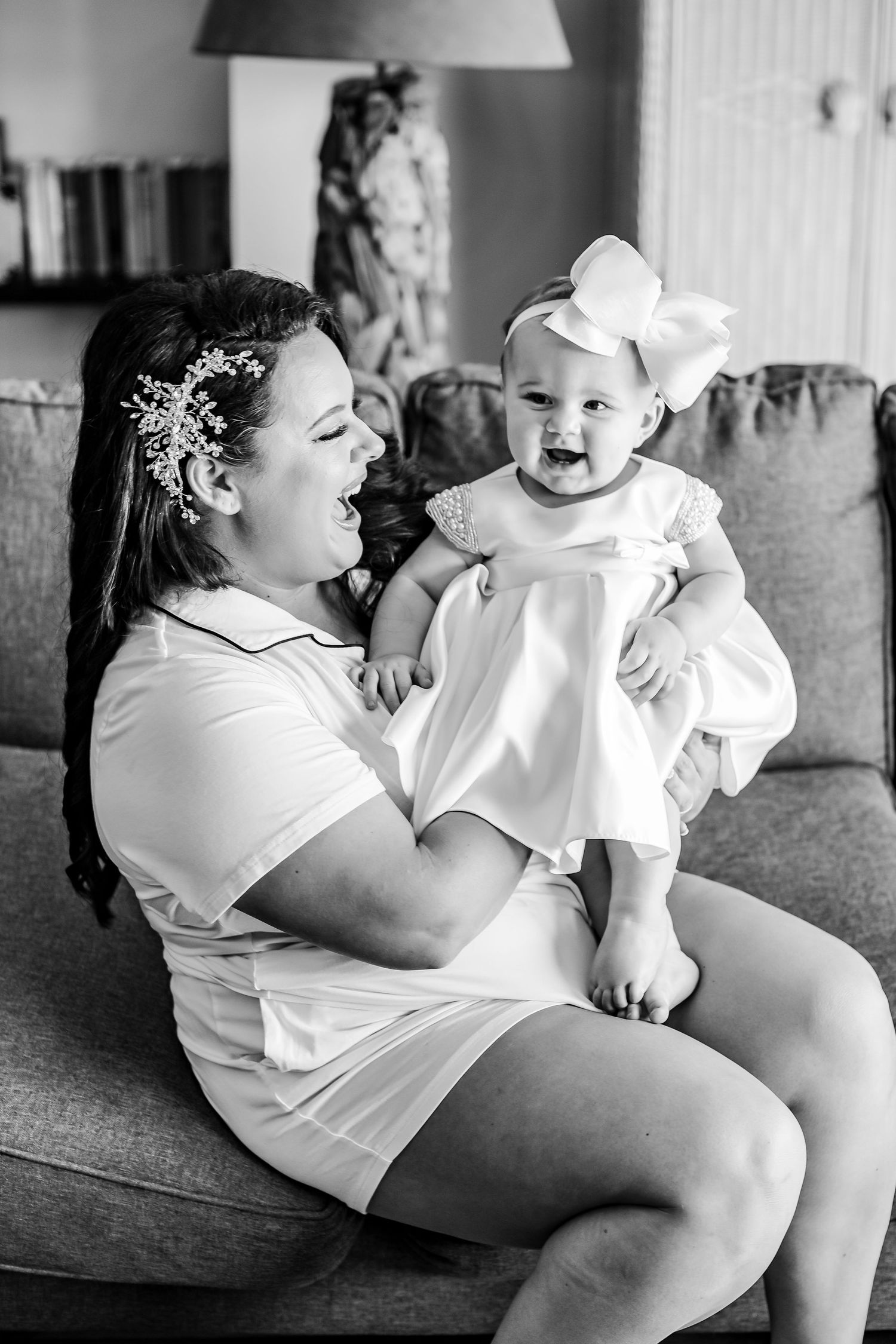 A sweet moment between parent and baby in white outfits sitting on a gray couch.