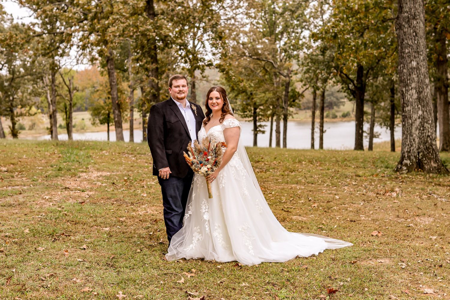 Autumn wedding portrait of couple standing in front of a lake with fall foliage.