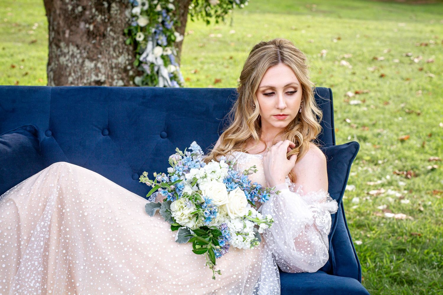 Romantic bridal portrait on blue velvet sofa with delicate lace gown and spring bouquet.