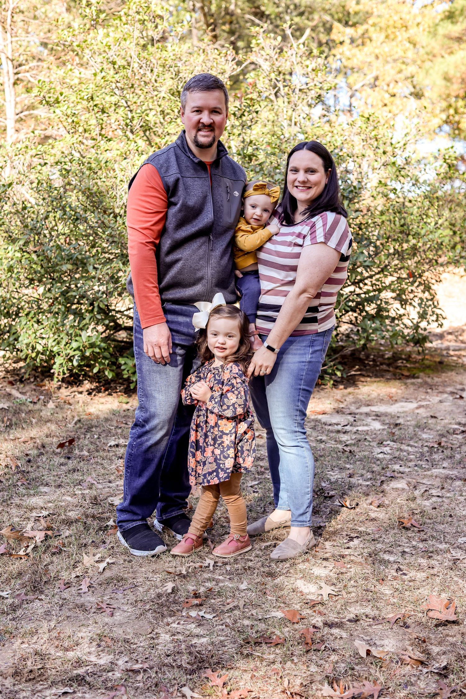 Family of four poses together outdoors in casual clothing during autumn.