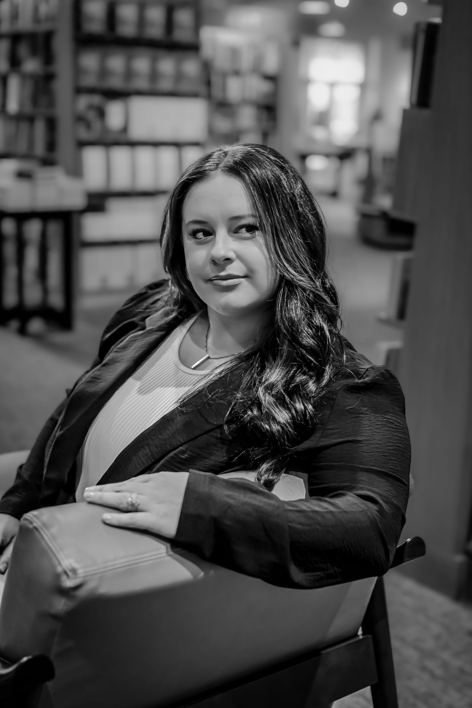 Professional portrait in black blazer seated in library setting.