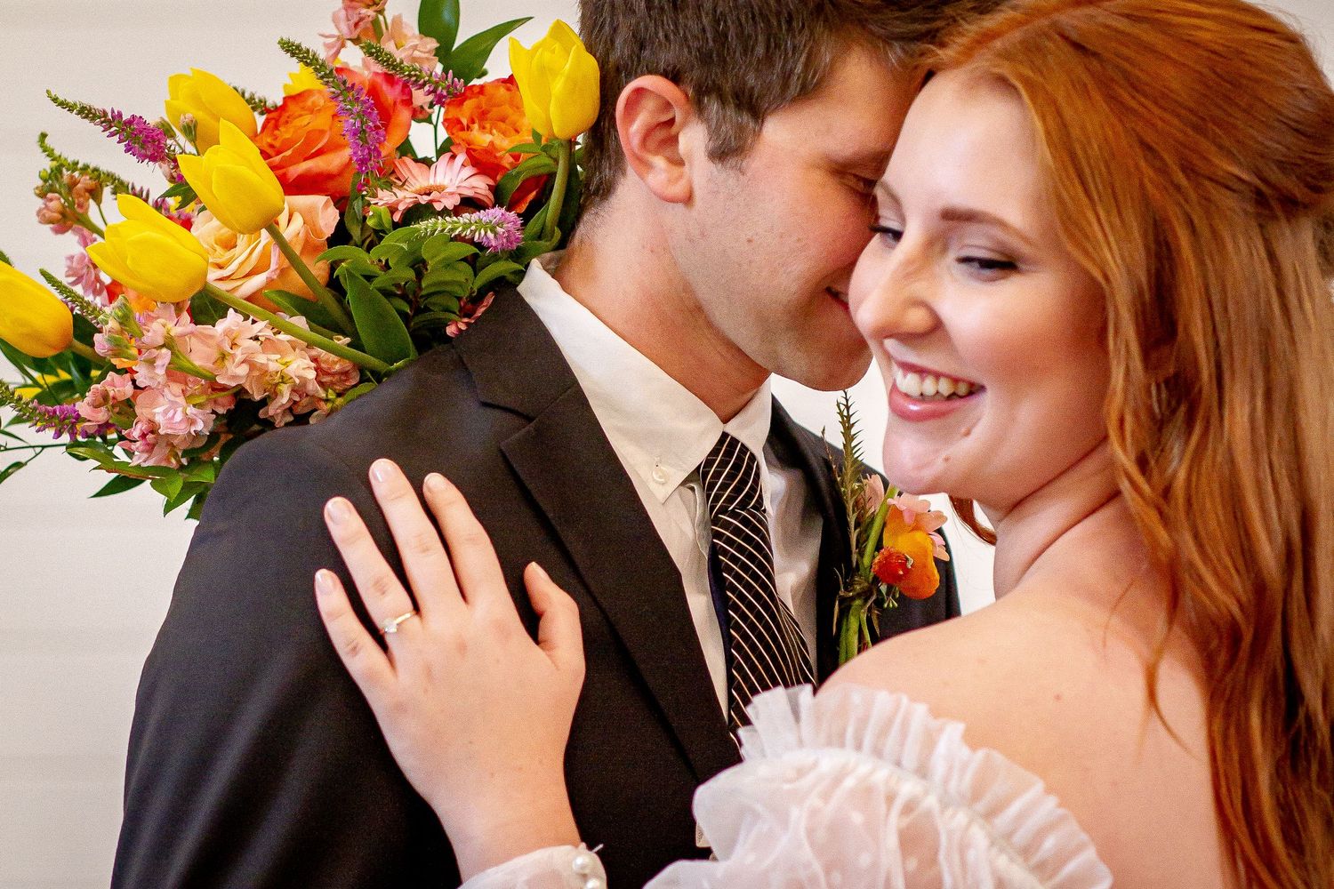 A romantic wedding moment with bright yellow and orange floral arrangements in the background.