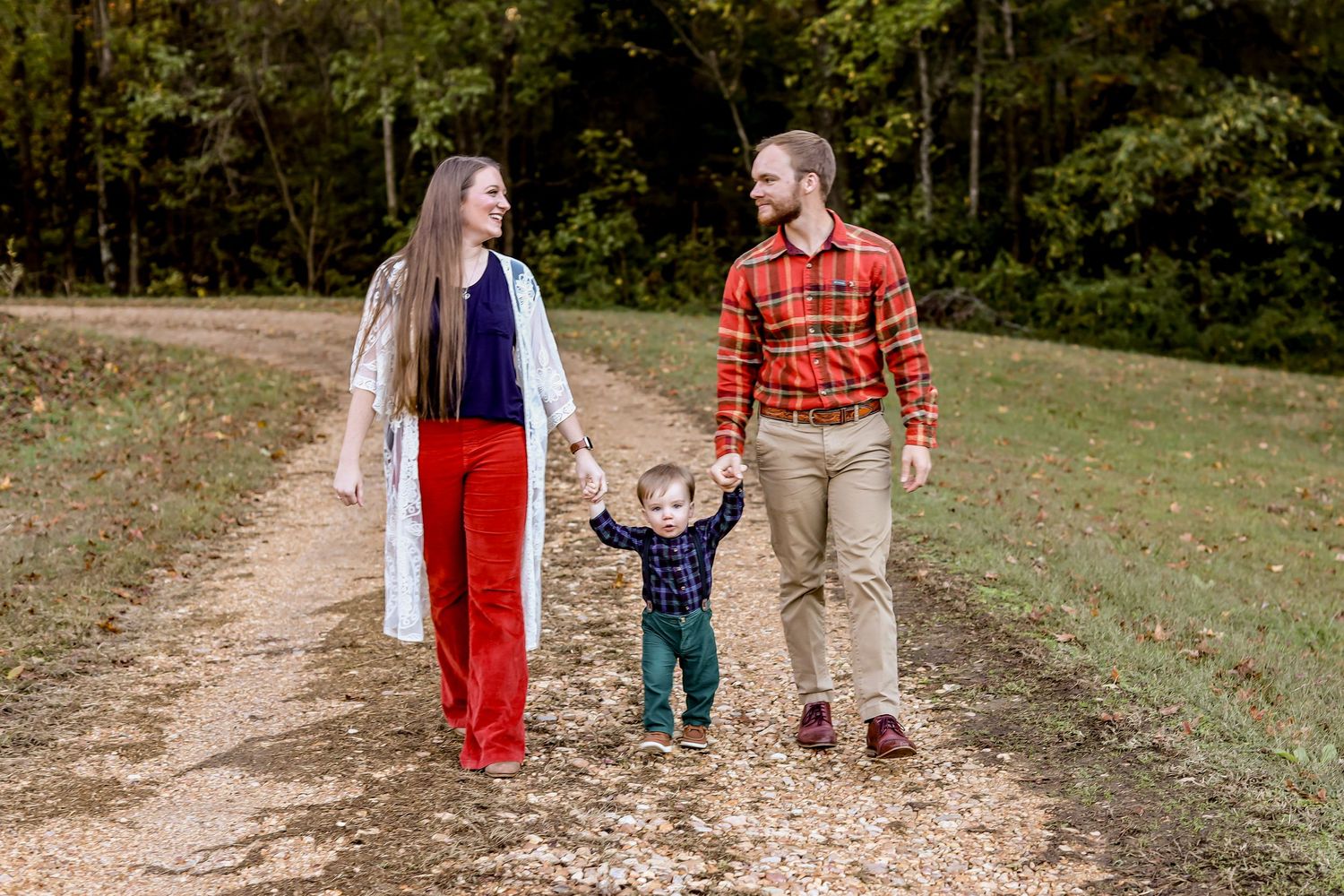 Family walking together on autumn trail through wooded area with fall foliage.