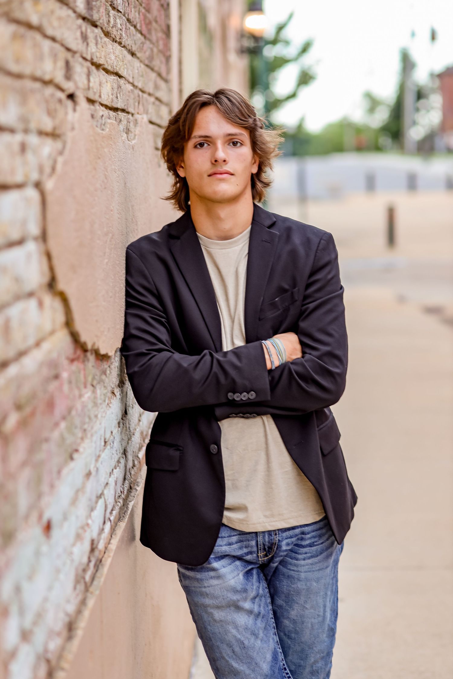 Casual portrait against brick wall wearing dark blazer and jeans in urban setting.