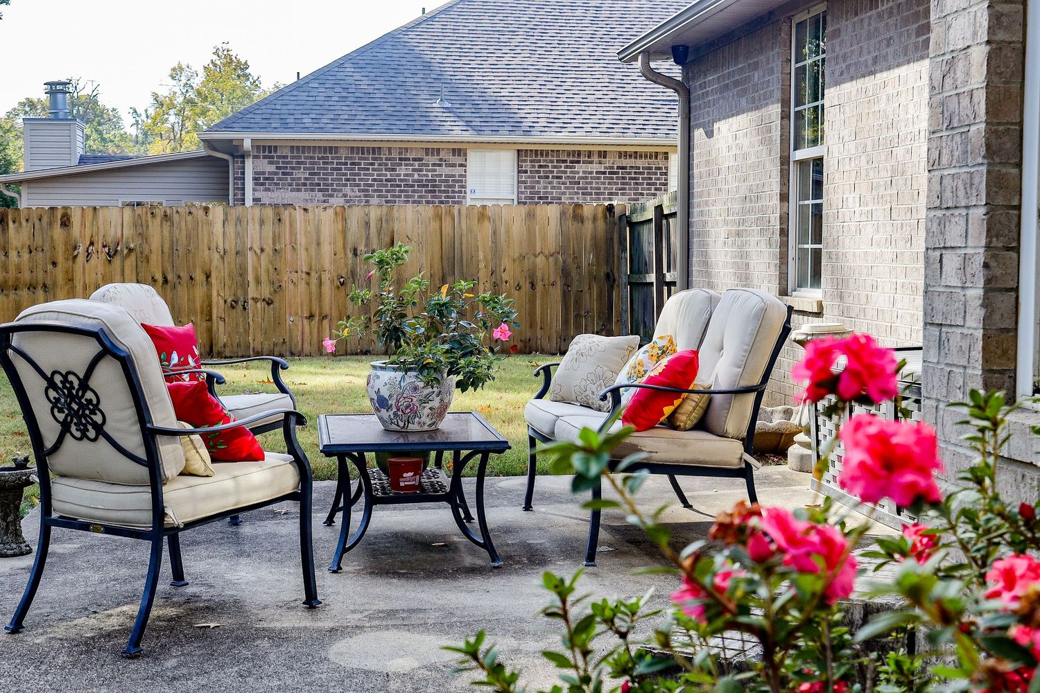 Outdoor patio furniture set with red cushions and decorative flowers on a stone patio.