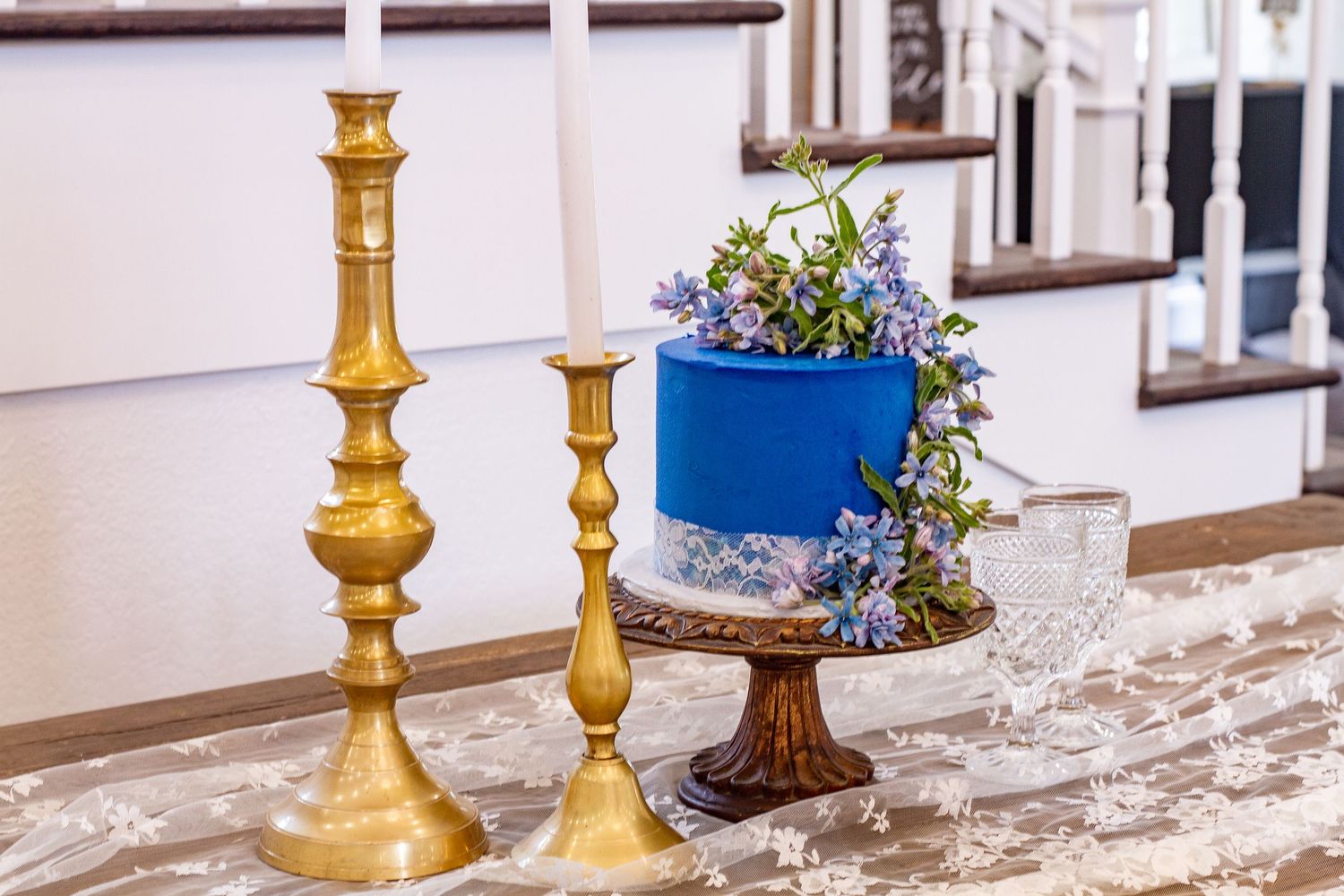 Elegant table setting with gold candlesticks and blue floral centerpiece on marble surface.