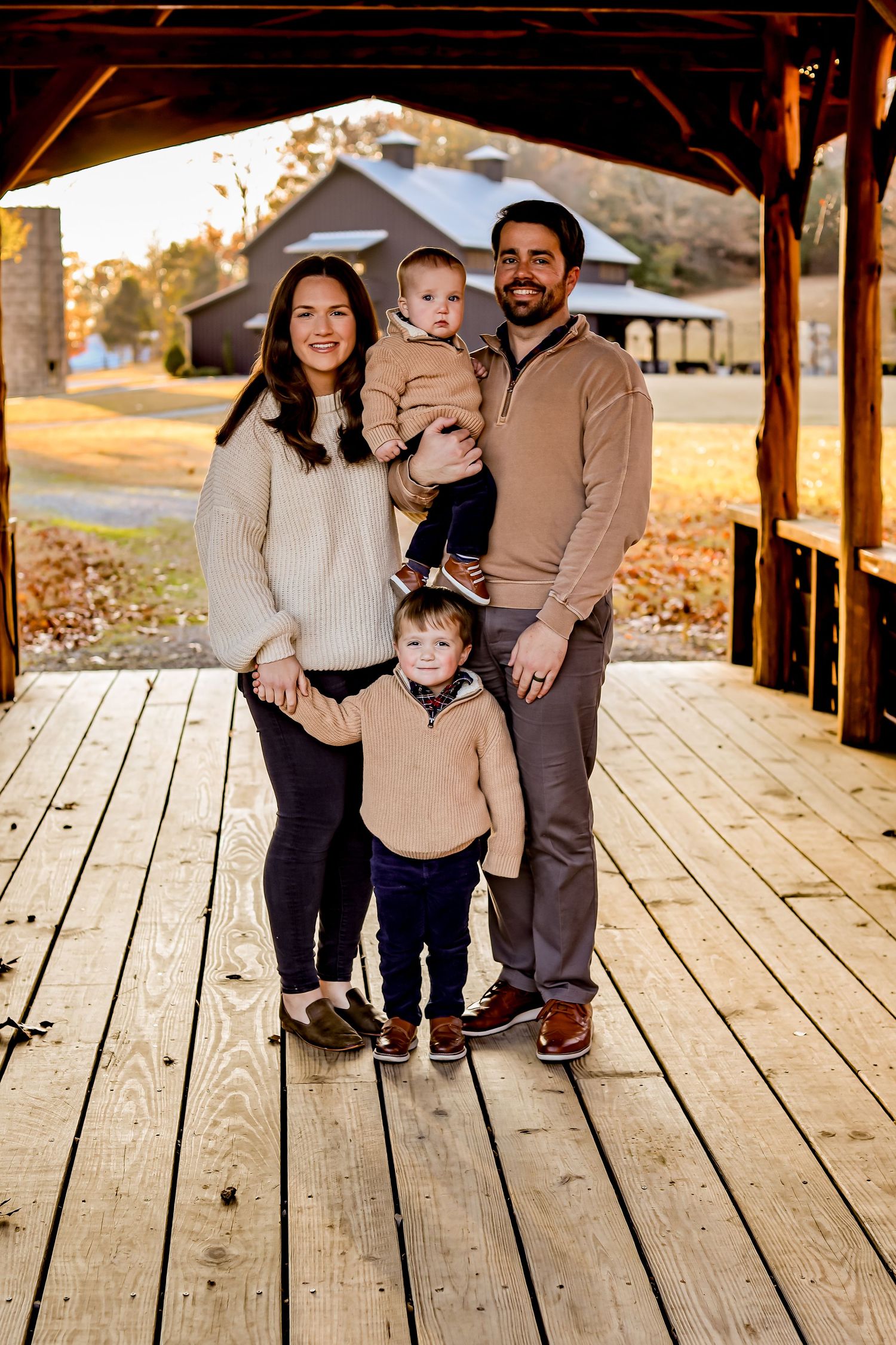 Family portrait on wooden deck with rustic barn in background during golden hour.