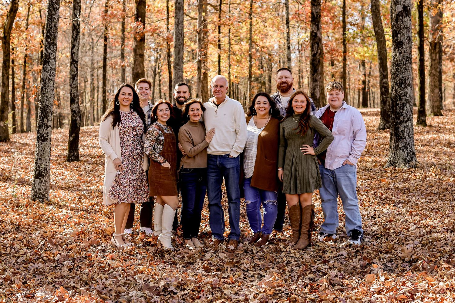 Large family group poses together among fall foliage in wooded setting.