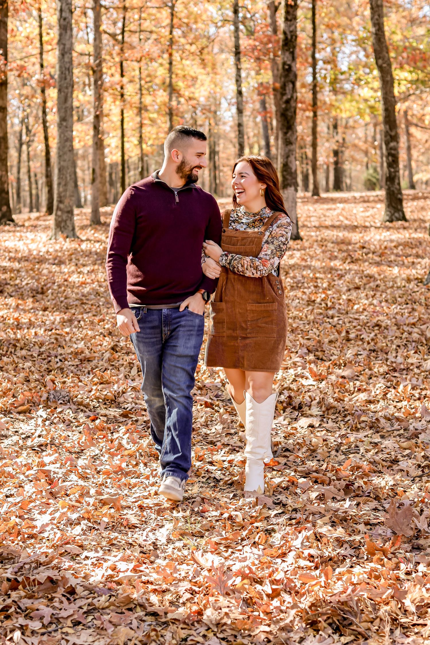 Couple walking through fall foliage covered ground in wooded area during autumn photo session.