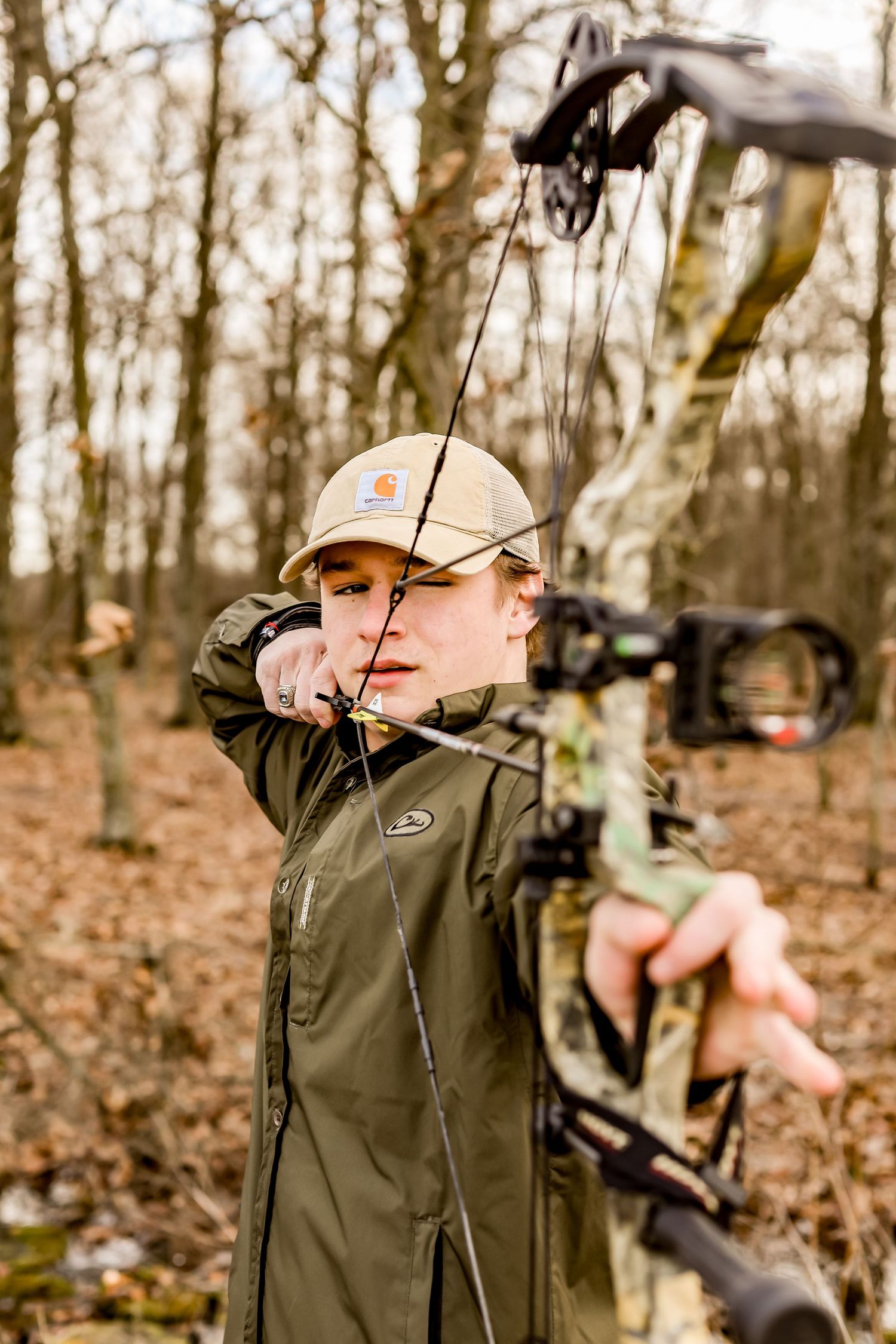 Person practicing archery with a compound bow in a wooded forest setting.