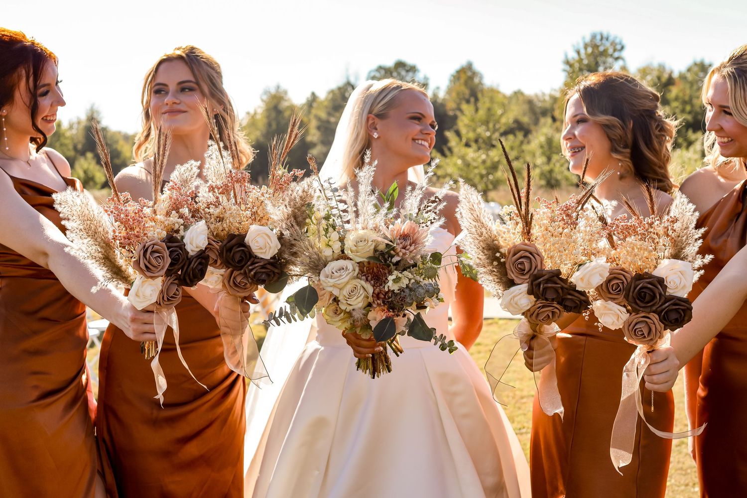 Wedding party holding bouquets in golden sunlight outdoors.