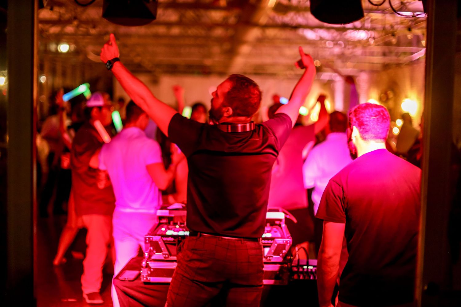 DJ performs at a nightclub with red lighting and dancing crowd silhouettes.