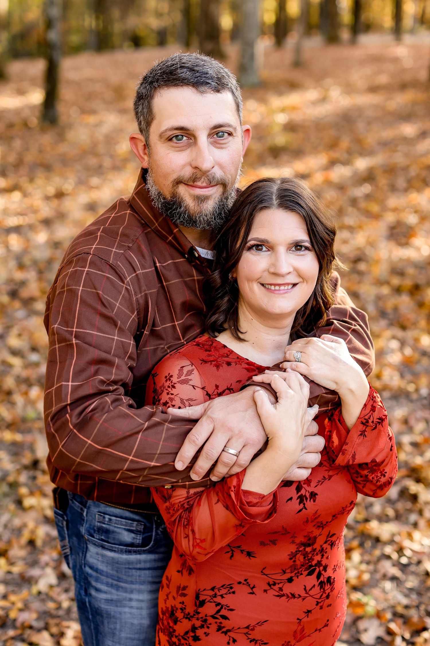Couple embraces while posing for portrait in autumn forest setting.