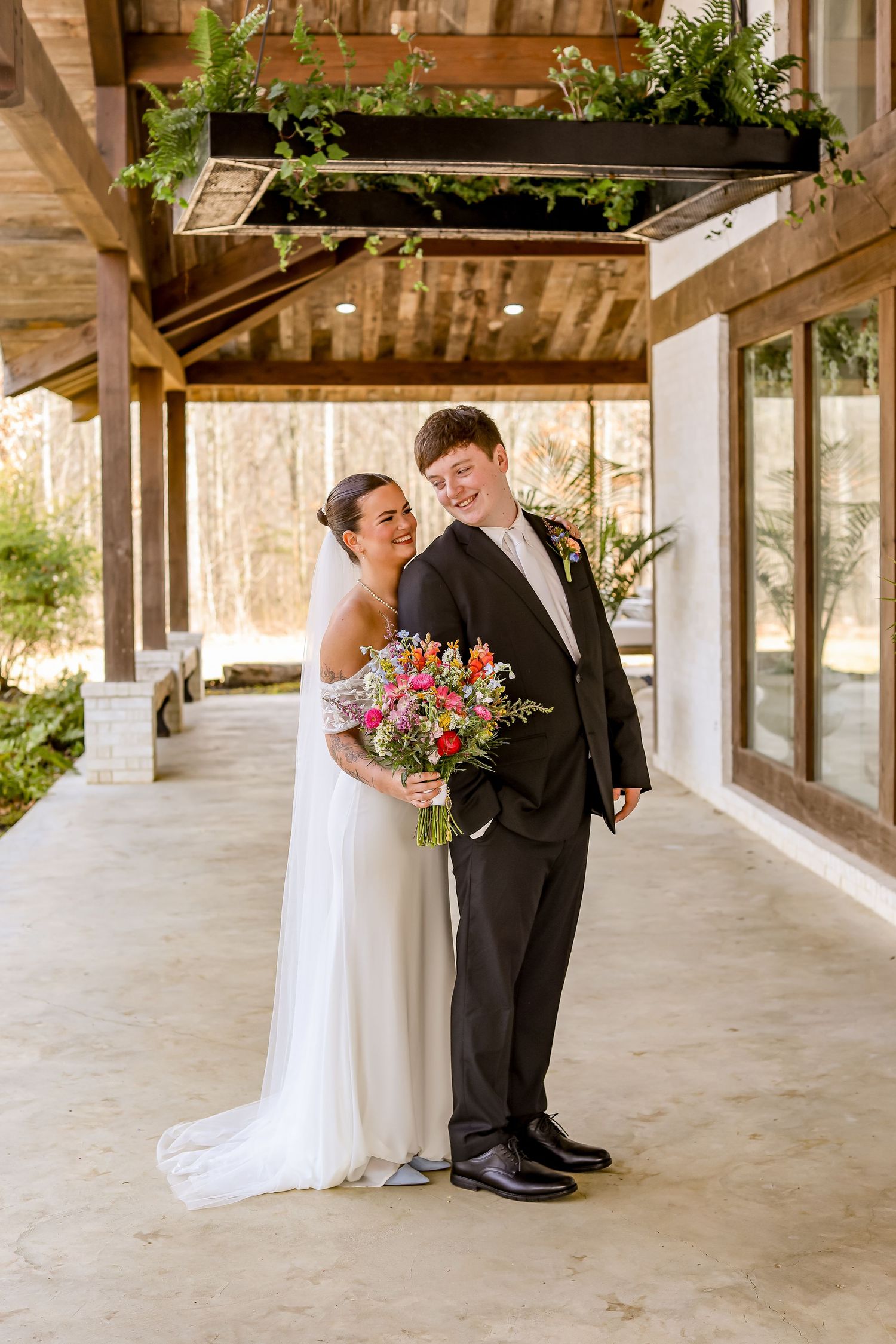 Newlyweds share a moment under a wooden pergola with a colorful spring bouquet.