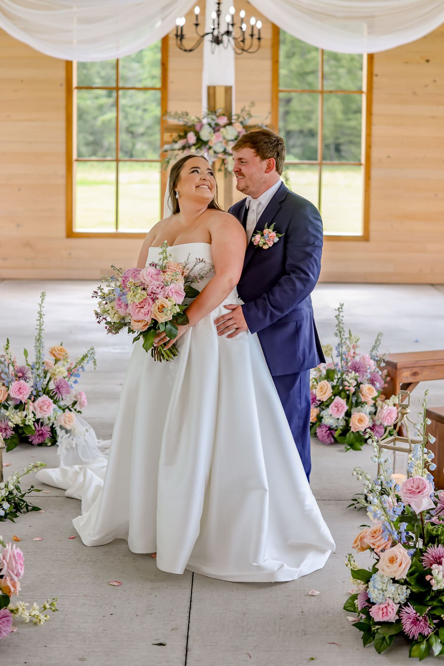 A couple dances in an elegant barn venue decorated with white drapes and floral arrangements.