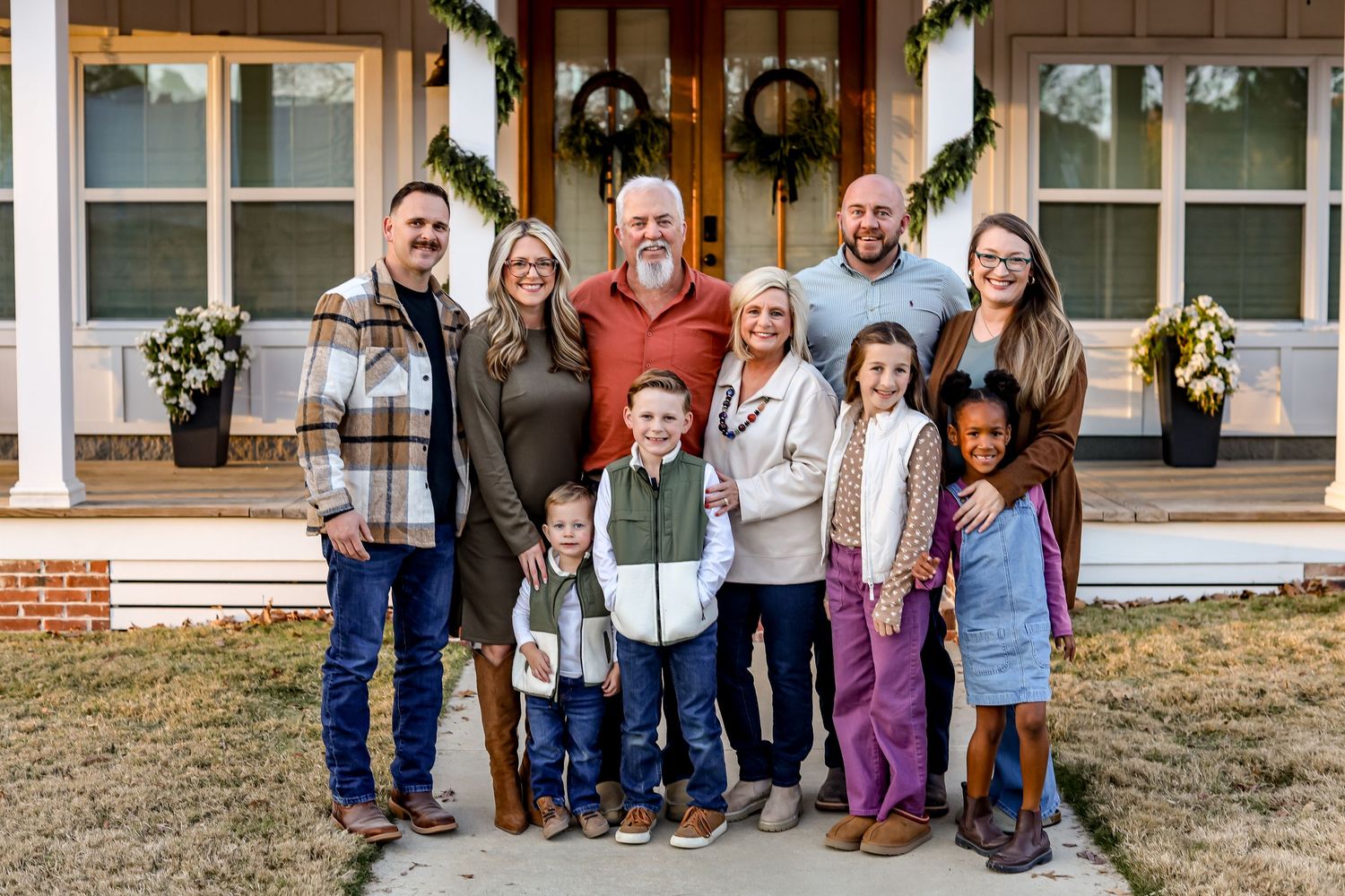 Group photo on front porch steps with holiday greenery garland decorating the doorway behind them.
