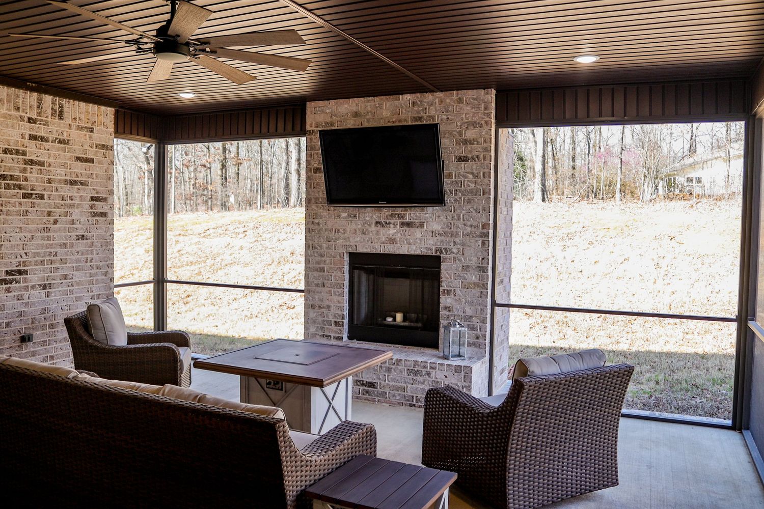Covered outdoor patio with brick walls and comfortable seating overlooking wooded area.