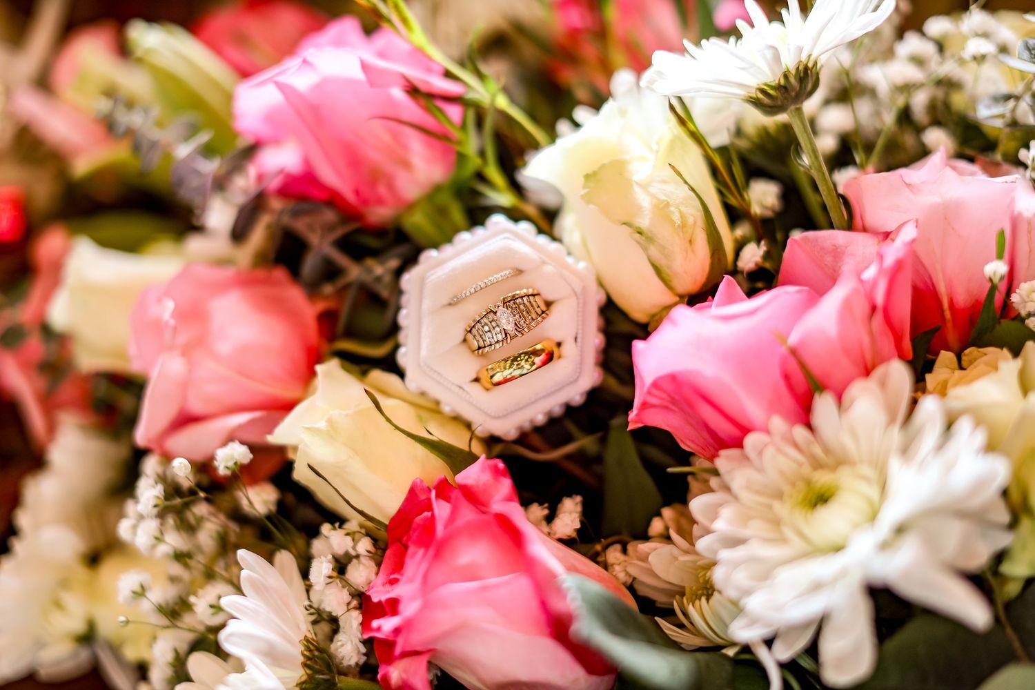 A close-up of wedding rings nestled among pink roses and white flowers in a bouquet.