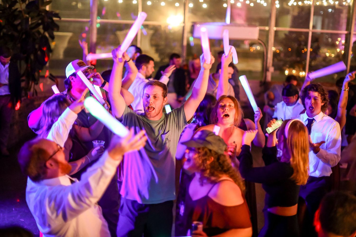 Crowd celebrates with glowing light sticks on a dark dance floor.
