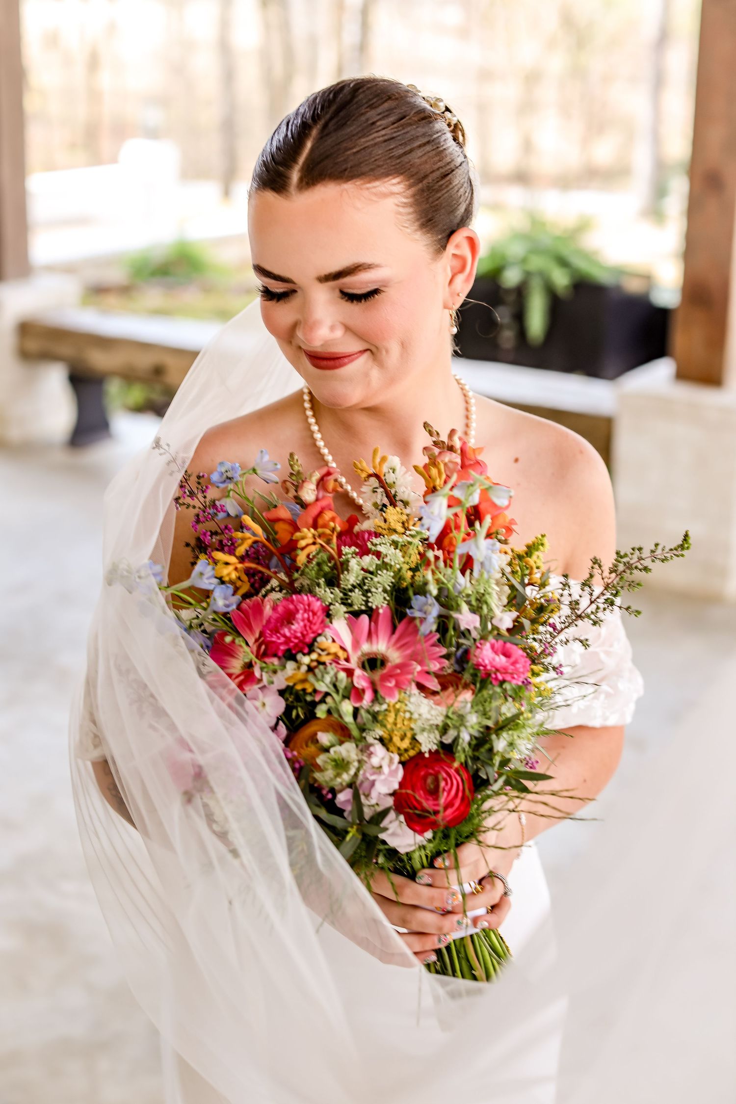A bride in a white dress smiles while holding a vibrant wildflower bouquet with pink and orange blooms.