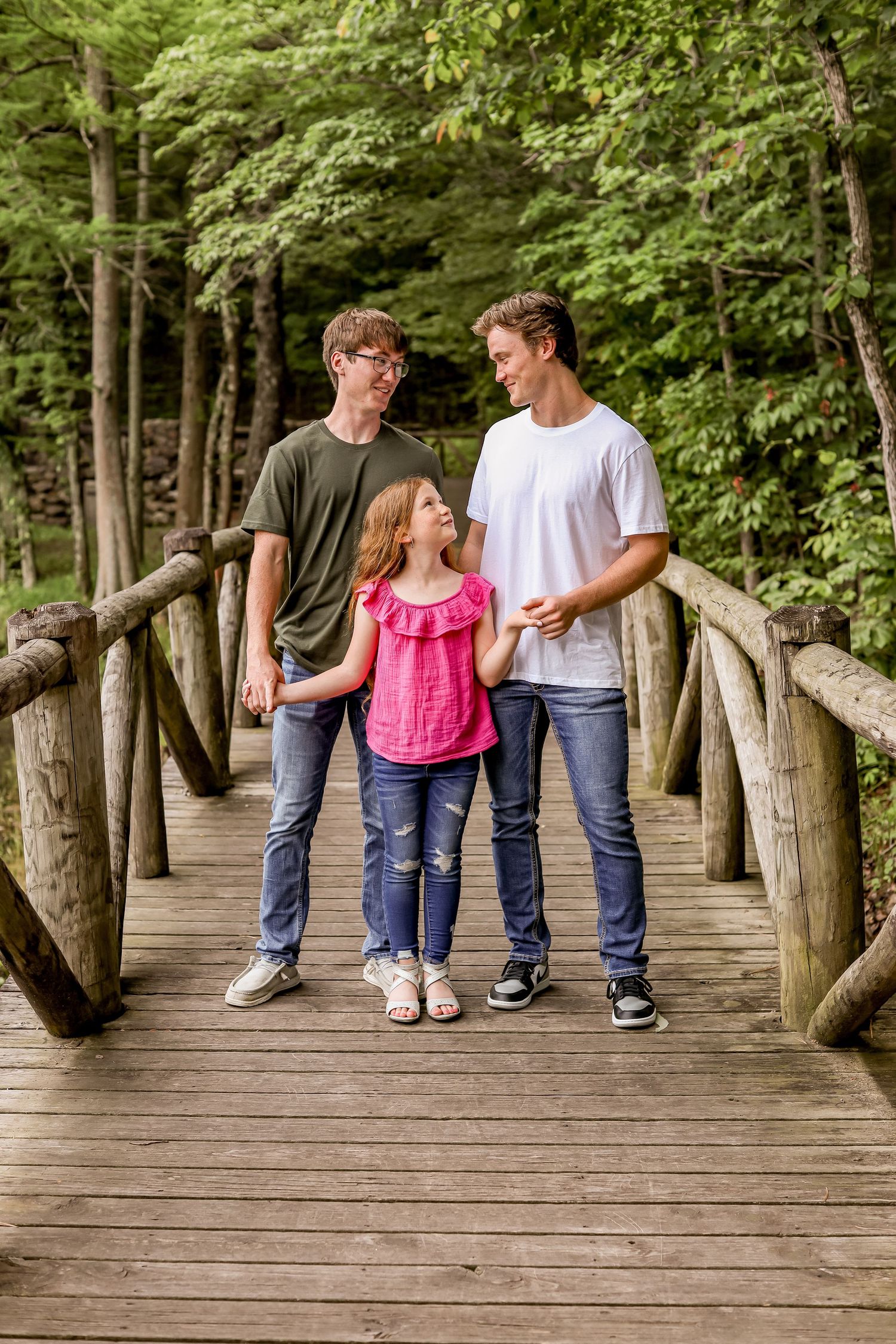 Three people walking together on rustic wooden bridge in lush forest.