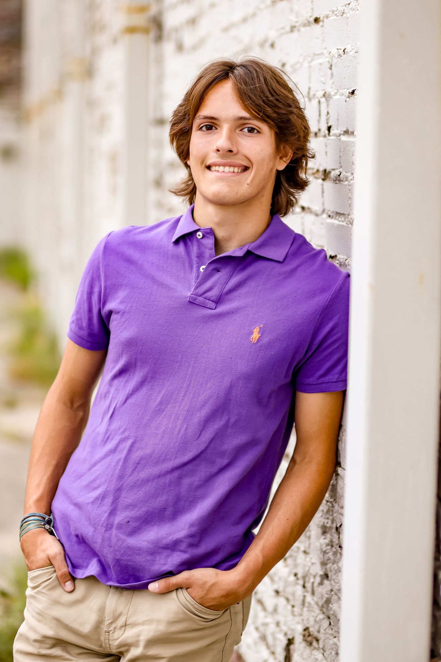 Portrait series of person in purple polo shirt leaning against white column outdoors.