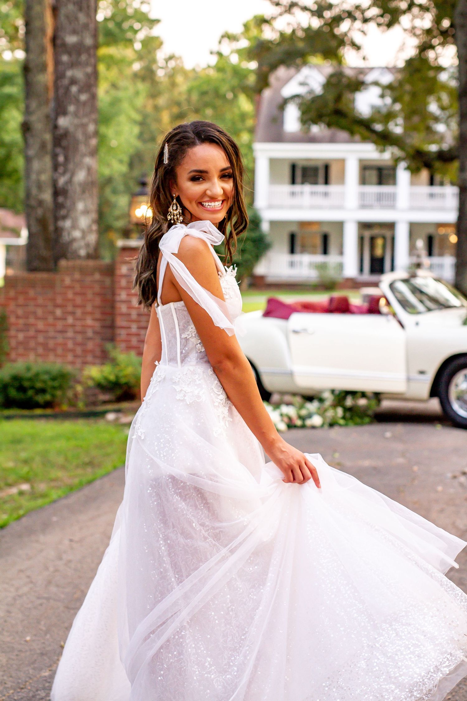 Elegant white wedding dress with flowing tulle skirt photographed outdoors on a driveway.