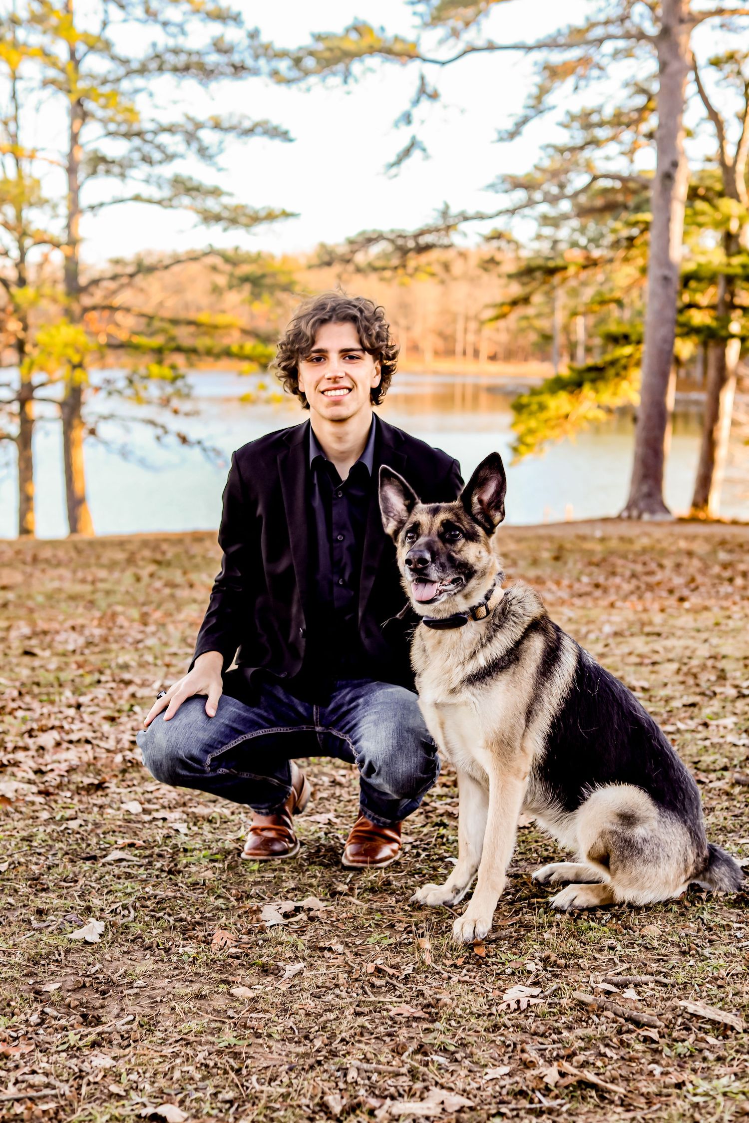 Person in black jacket with German Shepherd dog by lakeside in fall setting.